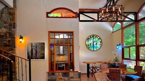 A spacious interior with a stone fireplace, wicker furniture, and large windows offering natural light.