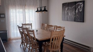 Un coin repas avec une table et des chaises en bois, un luminaire suspendu et un tableau au mur.