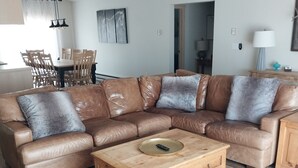 Un salon moderne avec un canapé d’angle en cuir marron, une table basse en bois et un tapis en peau de vache.