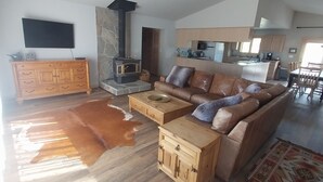 Un vaste salon doté d’un haut plafond, d’un ventilateur de plafond, d’une cheminée en pierre, d’un canapé en cuir, d’une table basse en bois et d’un téléviseur fixé au mur.