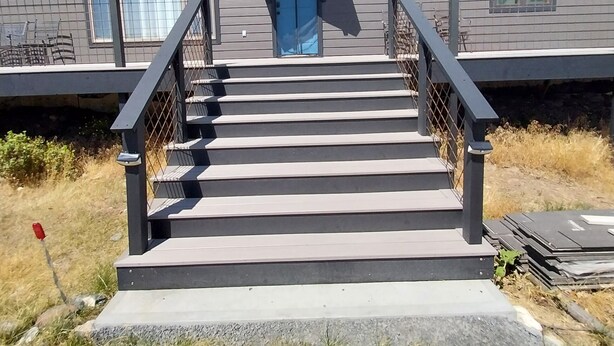 Un bâtiment à deux étages, à la façade grise, avec une porte bleue et un escalier menant à l’entrée.