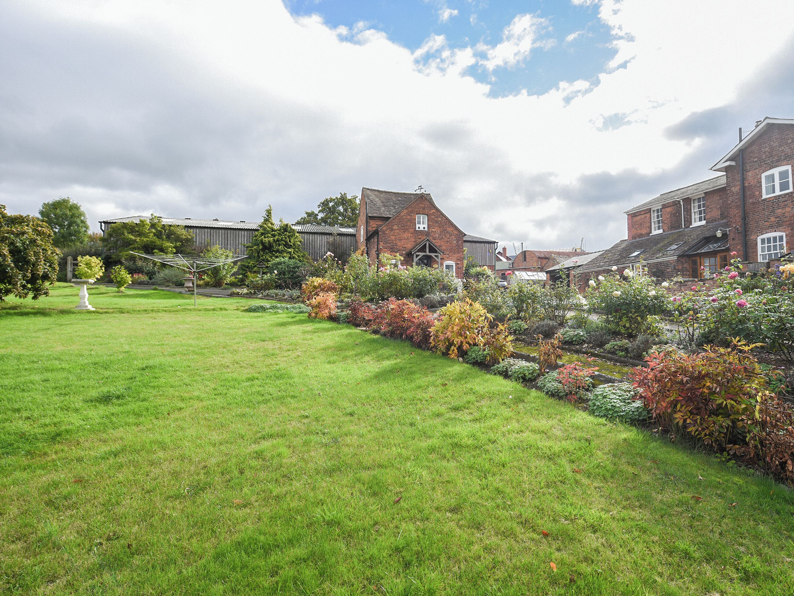 A residential area with a well-maintained lawn, a variety of flowering shrubs, and brick houses with pitched roofs.