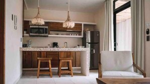 Eine moderne Küche mit Holdekor-Schränken, einer Granit-Arbeitsplatte und einer eingebauten Mikrowelle. Zwei hölzerne Barhocker und ein weißer Stuhl sind vorhanden.