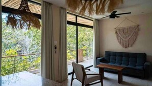 Ein Zimmer mit Balkon, Deckenventilator, einer Couch und einem hängenden Wandbehang aus Makramee.