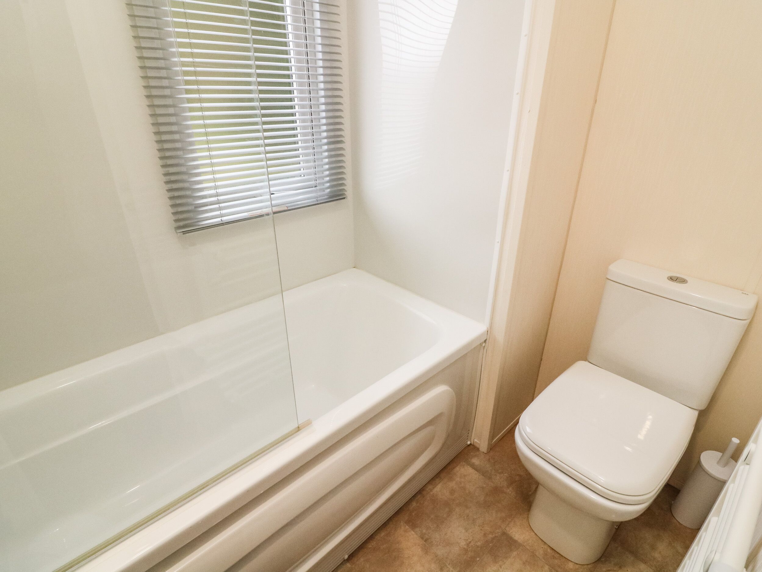 Une salle de bain avec une baignoire, des toilettes et une fenêtre avec des stores.