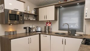 A modern kitchen with white cabinets, a stainless steel microwave, a toaster, and a sink. - 3 Yealands (Carnforth)