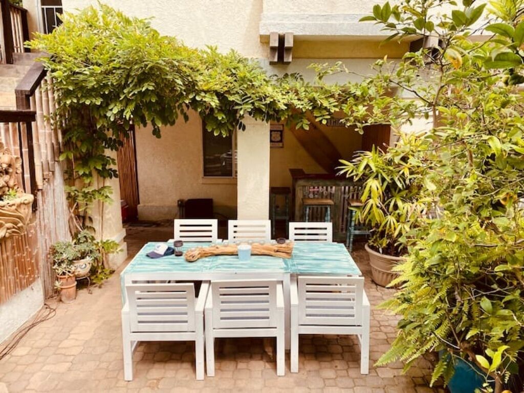 A patio with a table and chairs, surrounded by potted plants and a pergola.
