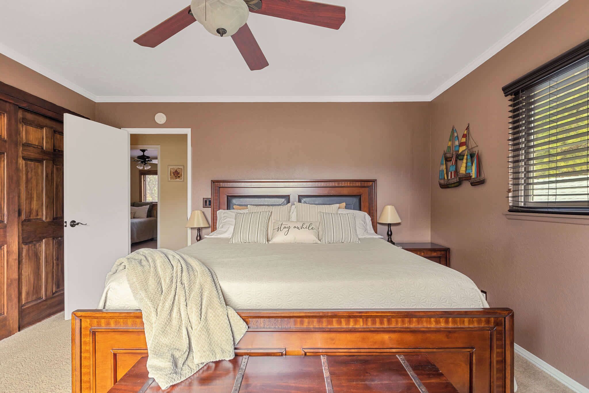 A bedroom with a wooden bed, two bedside lamps, a ceiling fan, and a window with blinds.