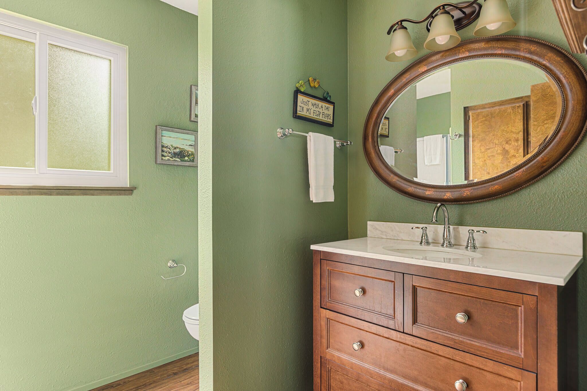 A bathroom with a green wall, a wooden vanity with a mirror, and a window with frosted glass.