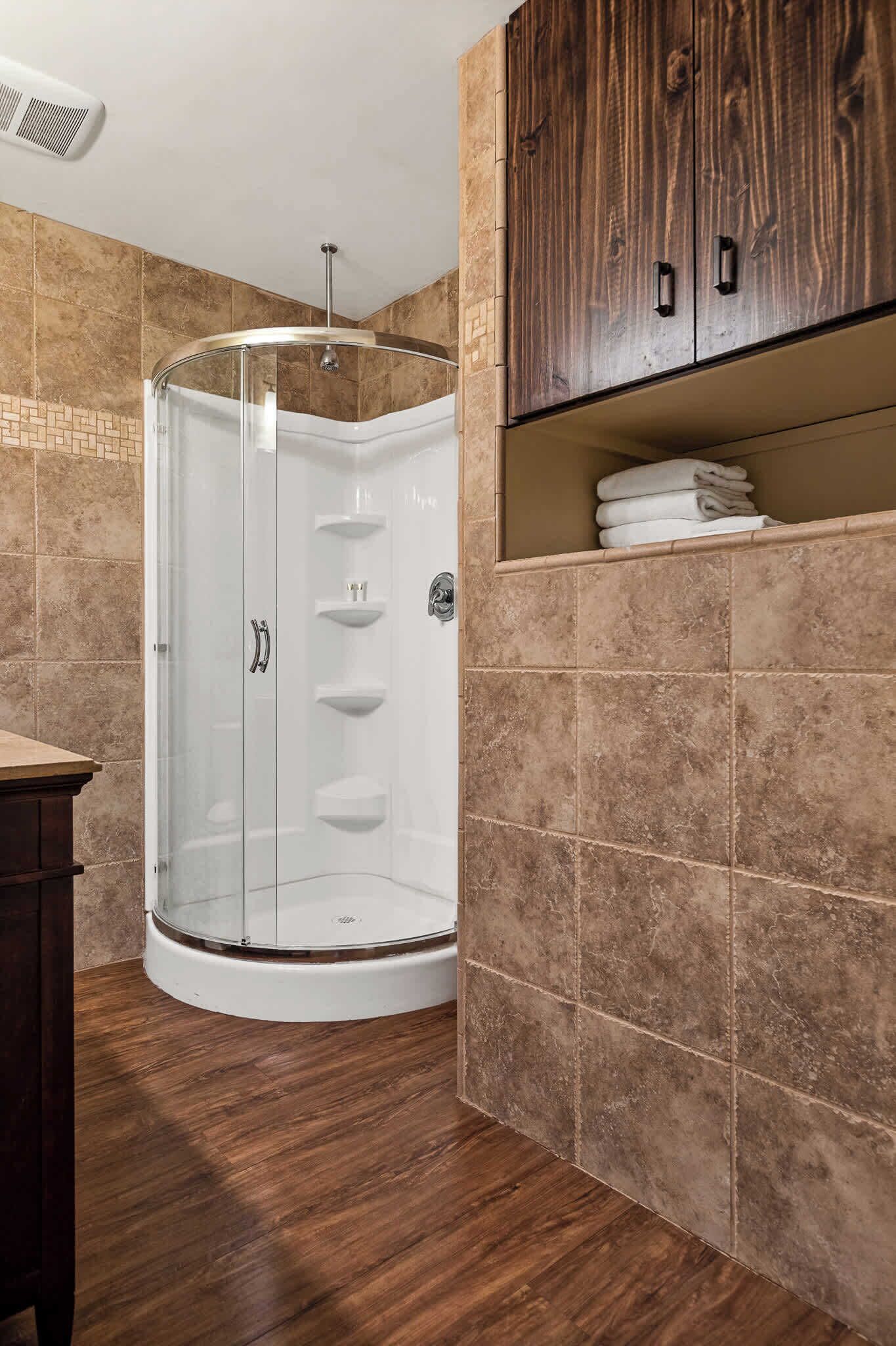 Baño con cabina de ducha de vidrio, paredes de azulejos y un mueble de madera con toallas.