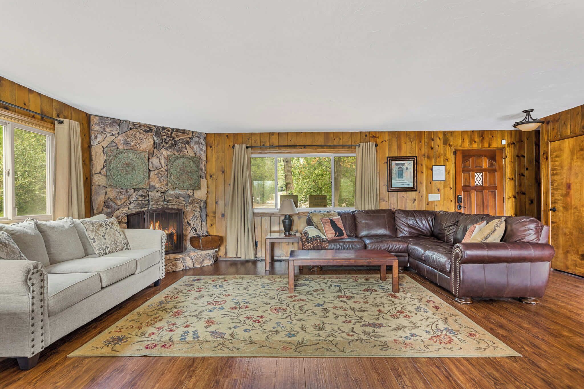 A cozy living room with a stone fireplace, a leather sofa, a wooden coffee table, and a floral rug.