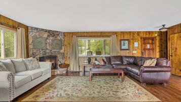 A cozy living room with a stone fireplace, a leather sofa, a wooden coffee table, and a floral rug.