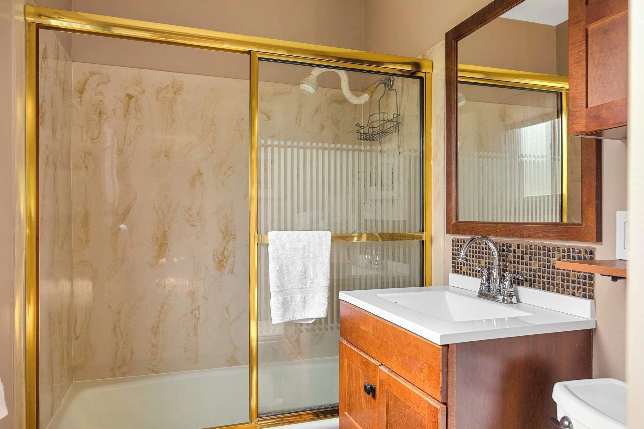Une salle de bain avec une douche à parois de verre, un lavabo blanc et un meuble-lavabo en bois.