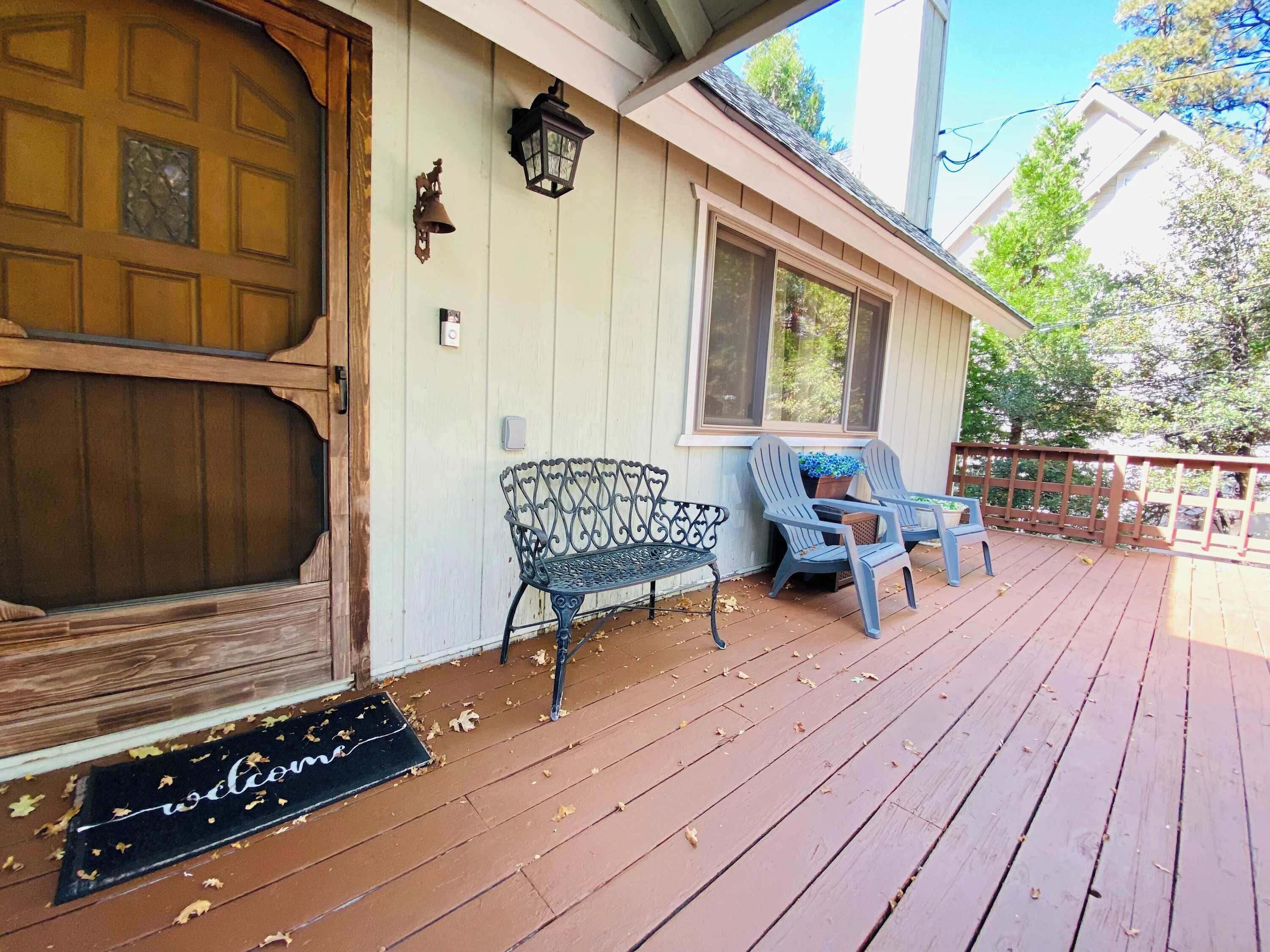 A wooden porch with a welcome mat, a bench, and two chairs.