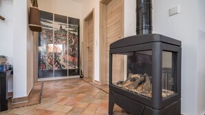 Un interior moderno con una estufa de leña, un vidrio que da a un balcón y piso de baldosas.
