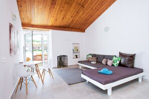 A modern living room with a white sofa, a dining area with a white table and chairs, and a wooden ceiling.