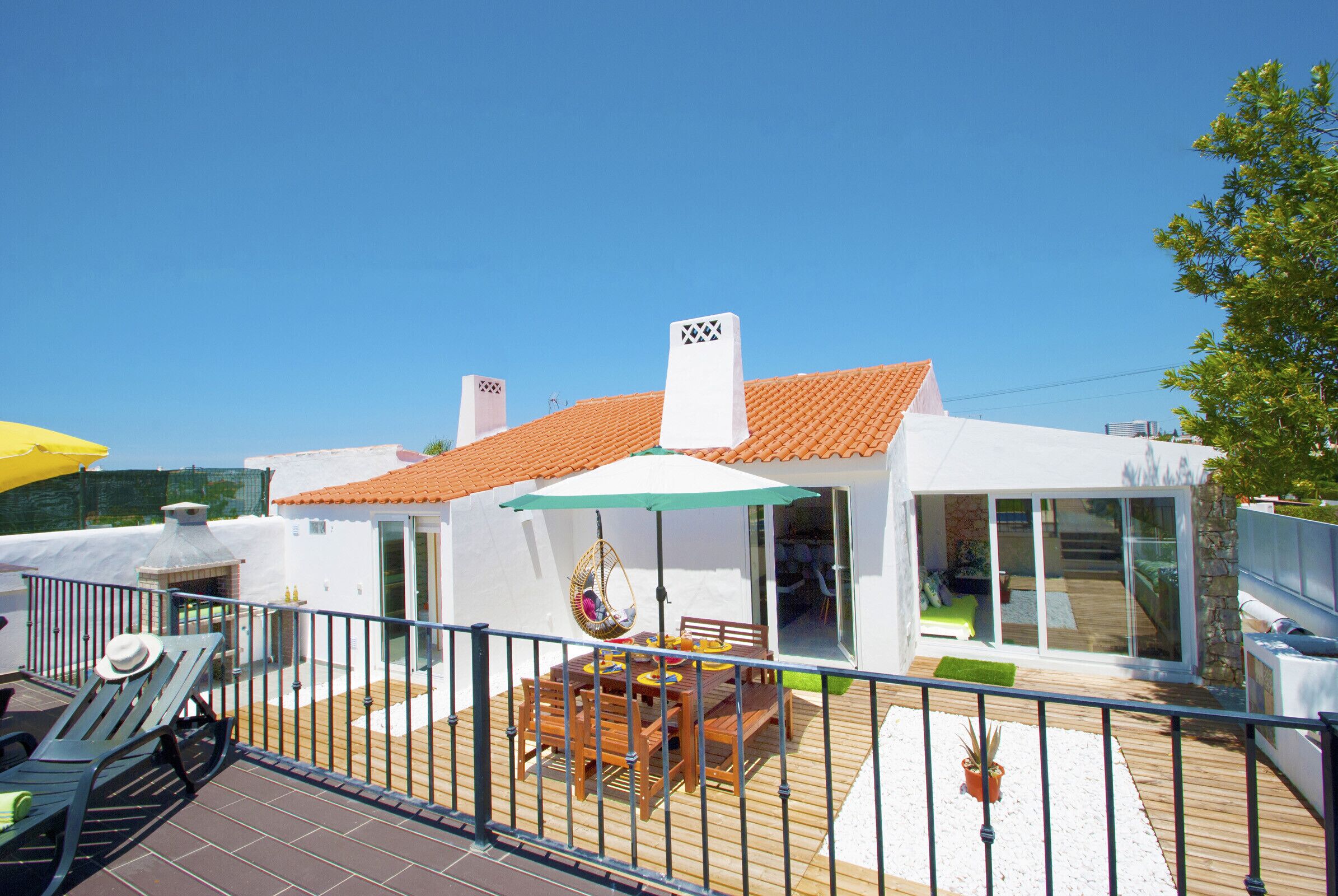 A modern house with a tiled roof, a patio with a table and chairs, and a hanging chair.
