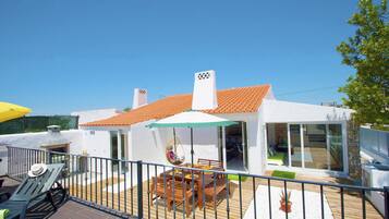 A modern house with a tiled roof, a patio with a table and chairs, and a hanging chair.