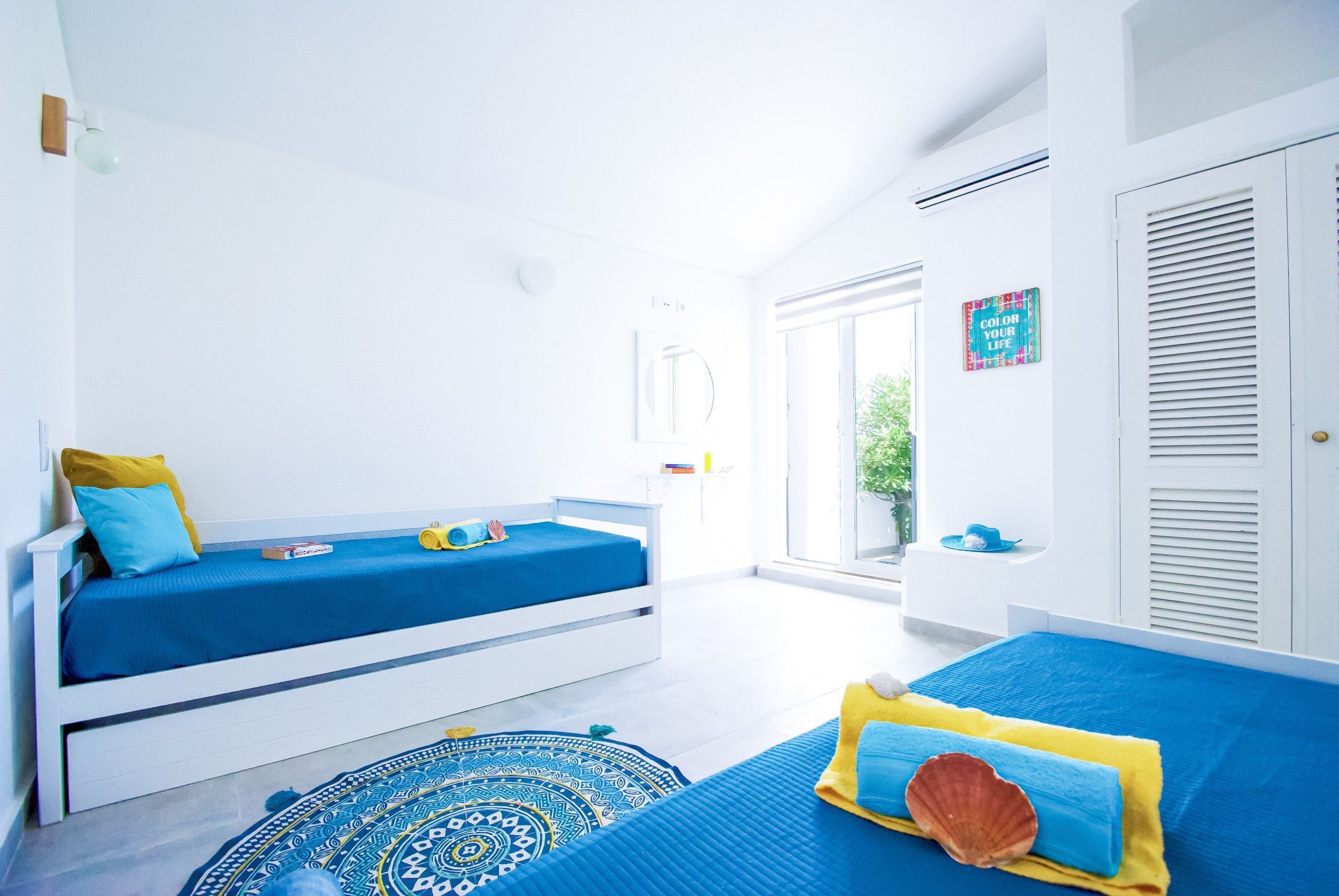 A bright, white room with two beds, a window, and a door.