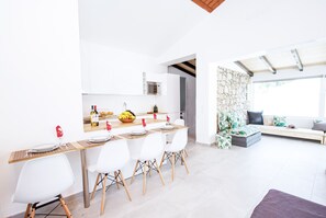Una cocina moderna con armarios blancos, una mesa de comedor para cuatro personas y una pared de piedra al fondo.