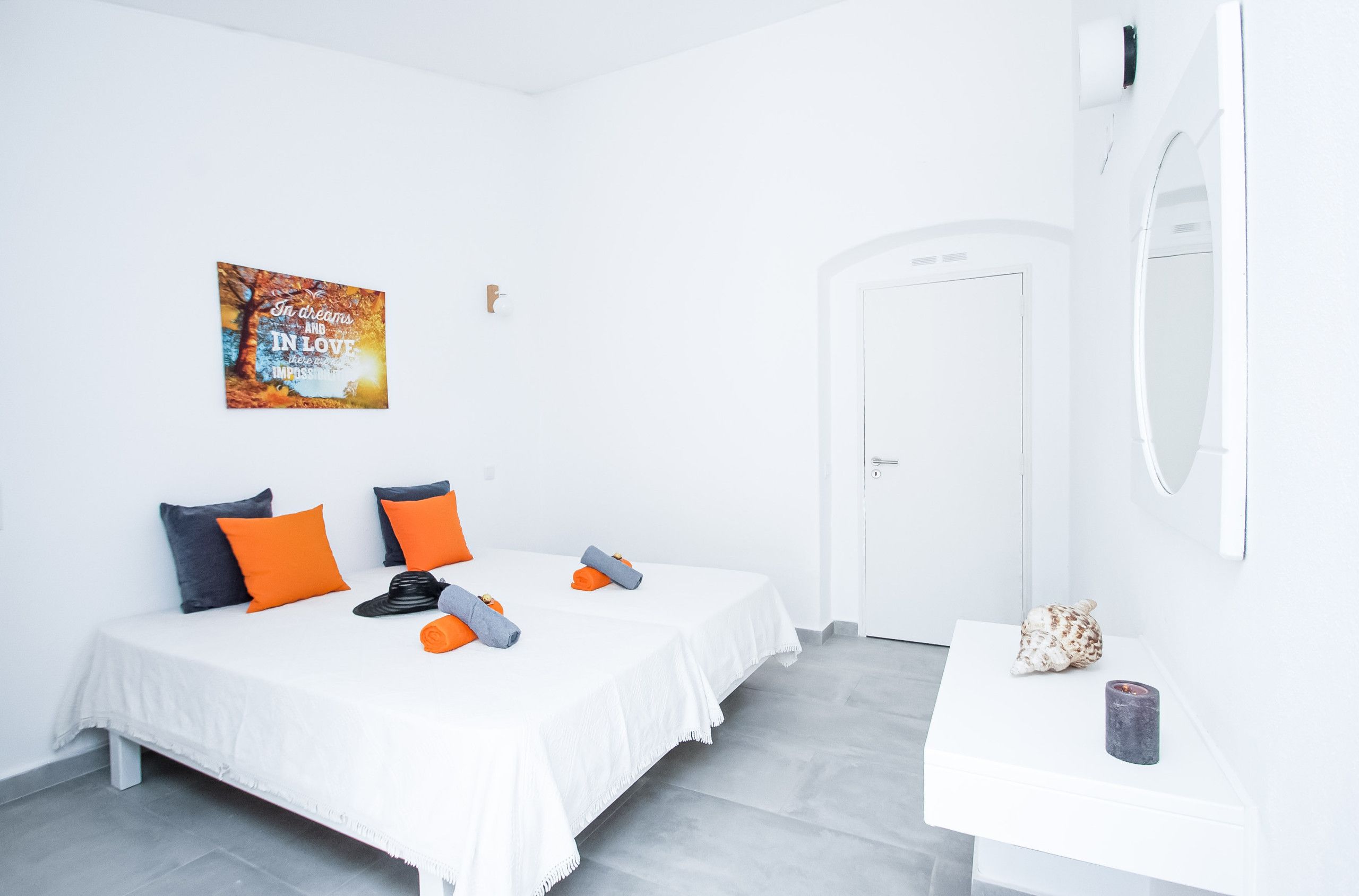 A hotel room with two beds, a white wall, a painting, a mirror, and a small table with a decorative item.