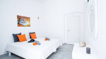 A hotel room with two beds, a white wall, a painting, a mirror, and a small table with a decorative item.