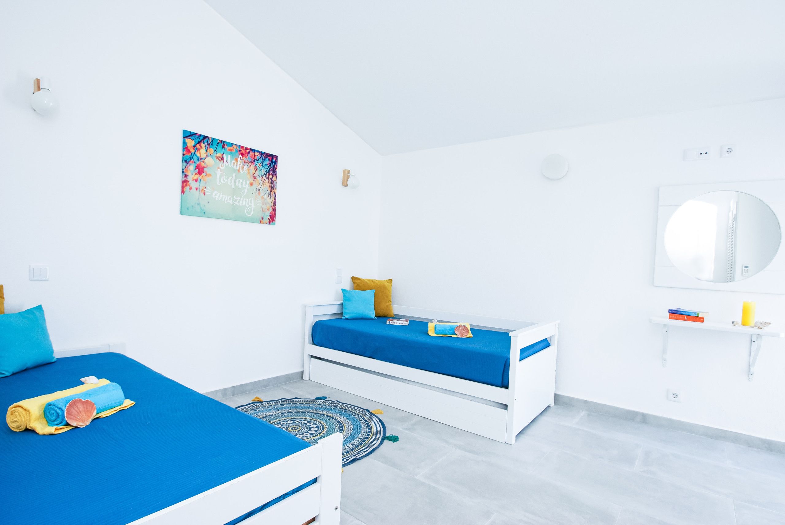 A modern bedroom with a bed, a smaller bed, a wall-mounted mirror, and a motivational poster.
