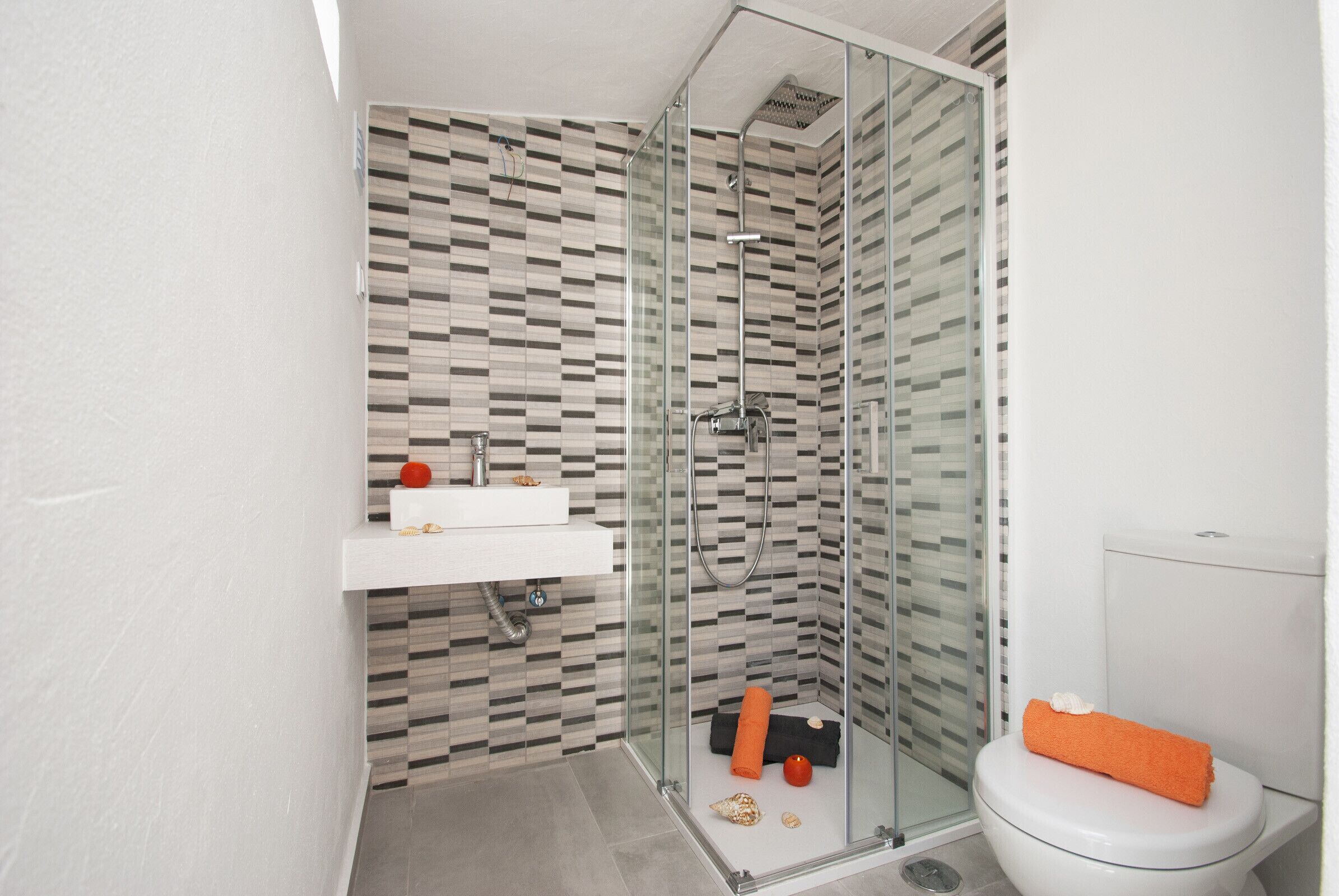 A modern bathroom with a glass shower enclosure, a white sink, and a toilet with an orange towel.