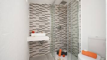 A modern bathroom with a glass shower enclosure, a white sink, and a toilet with an orange towel.