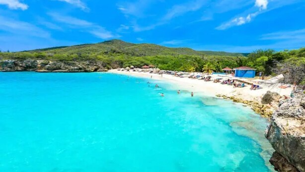 A beach with clear turquoise water, a sandy shore, and a few buildings in the background. - G Apartments (Willemstad)