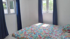 A bedroom with a bed, two windows with curtains, an air conditioning unit, and a view of greenery outside. - G Apartments (Willemstad)