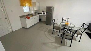 A compact kitchen with white cabinets, a refrigerator, and a dining area with a glass table and four chairs. - G Apartments (Willemstad)