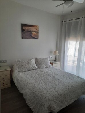 Quarto com uma cama, mesa de cabeceira, luminária, ventilador de teto e um quadro na parede.