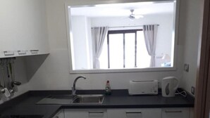 Une petite cuisine équipée d’une cuisinière, d’un évier et d’une fenêtre située au-dessus du plan de travail.
