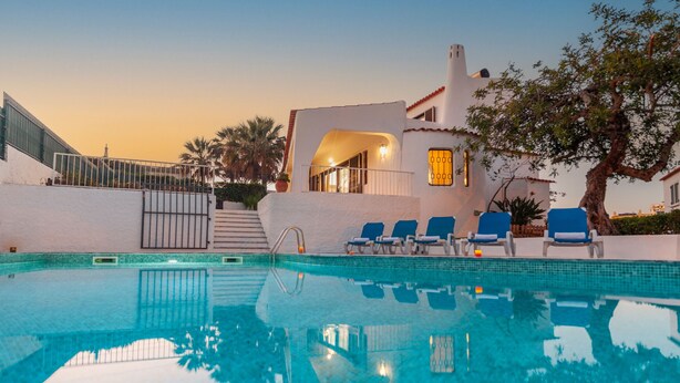 Une piscine avec des chaises longues, un bâtiment blanc doté d’un balcon et des palmiers.