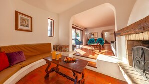Un salon avec un canapé, une table basse et une cheminée. On aperçoit à l’arrière-plan un coin repas avec des chaises et une table.