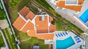 Vue aérienne d’un complexe hôtelier comprenant plusieurs bâtiments, une piscine et un court de tennis.