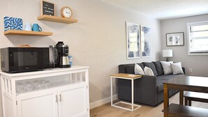 A compact living space with a kitchenette, a gray sofa, a small table, and a coffee machine.