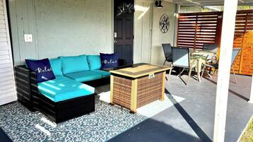 A covered outdoor seating area with a blue sofa, a small table, and a patterned rug.