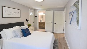 A bedroom with a bed, a bedside lamp, a framed quote on the wall, and a door leading to a bathroom.