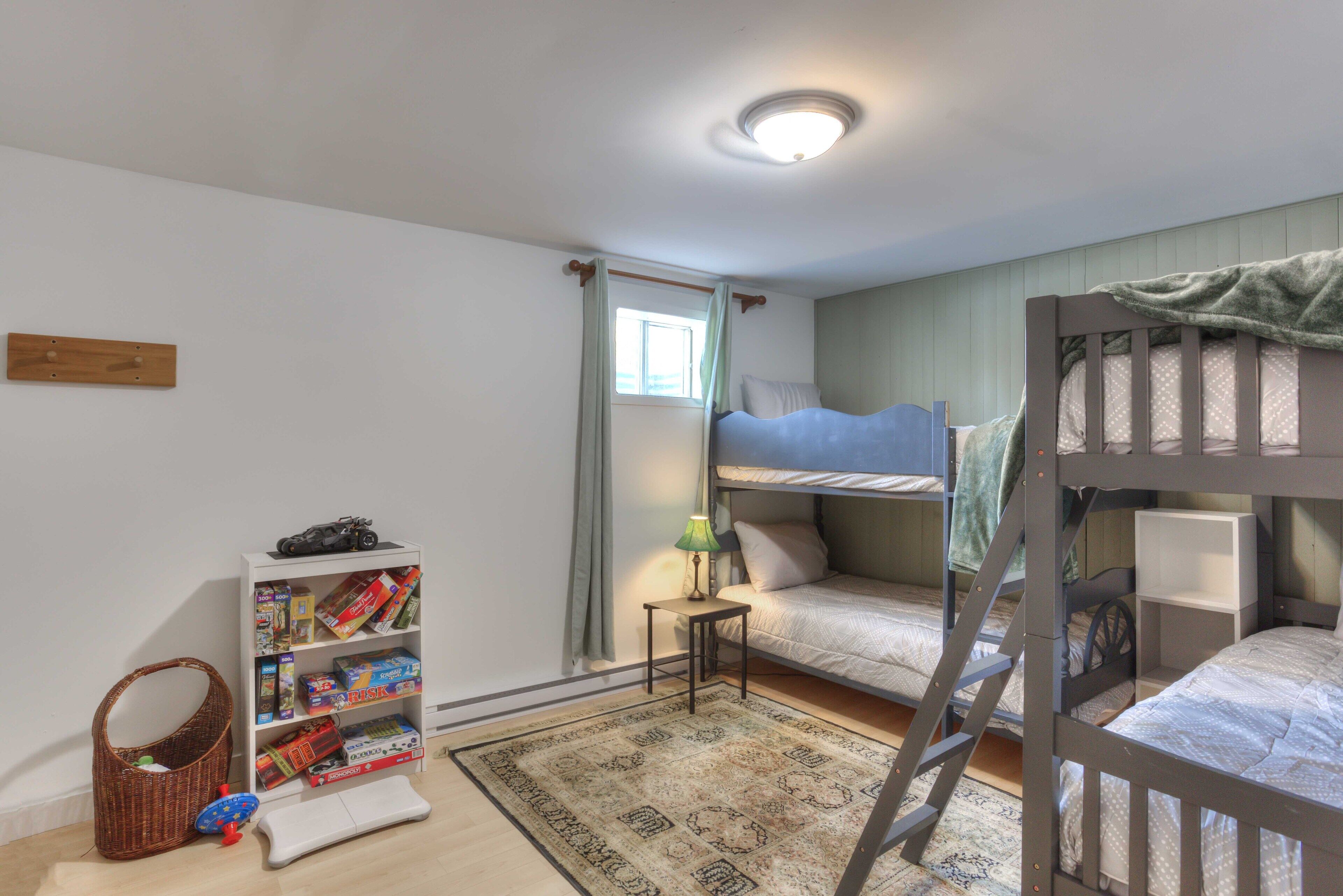 A child's room with bunk beds, a bookshelf, a small table with a lamp, and a patterned rug.