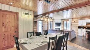 A dining area with a wooden table set for four, surrounded by chairs. A kitchen with a microwave and cabinets is visible in the background.