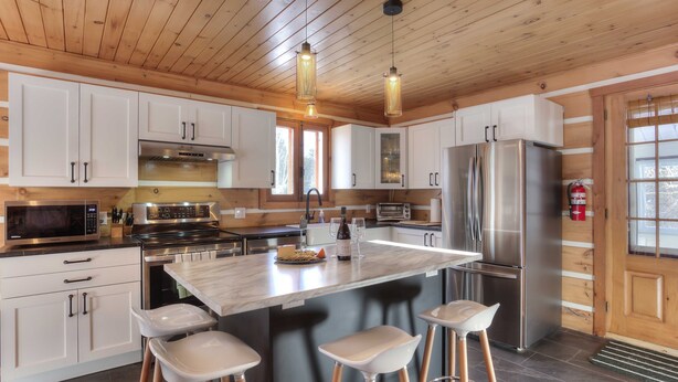 A modern kitchen with white cabinets, stainless steel appliances, a large island with bar stools, and pendant lighting.