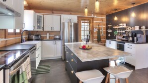 A modern kitchen with white cabinets, a stainless steel refrigerator, and a marble island with stools.