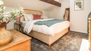 Un dormitorio con cama, cabecera de madera, tragaluz, mesita de noche, lámpara, espejo y planta en maceta.