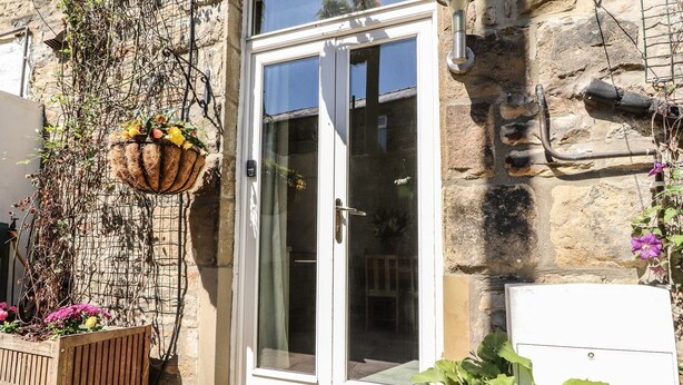 Un edificio de piedra con una puerta blanca, una maceta colgante con flores y una planta en maceta en la parte delantera.