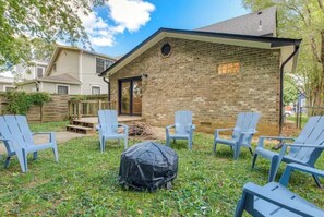 Relax on the covered porch with a grill at the center, surrounded by a grassy yard and a wooden fence.
