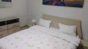 Un dormitorio con una cama, una mesita de noche, una lámpara, un aparador y dos cuadros en la pared.