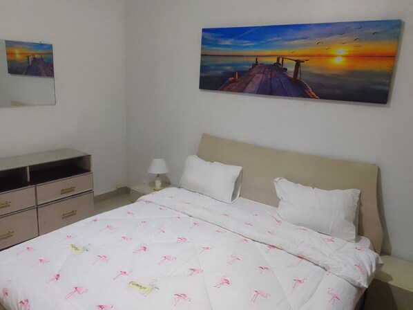 A bedroom with a bed, a nightstand, a lamp, a dresser, and two paintings on the wall.