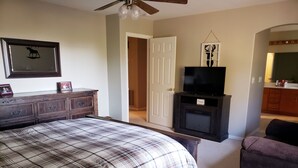 A bedroom with a bed, dresser, television, and a door leading to another room.